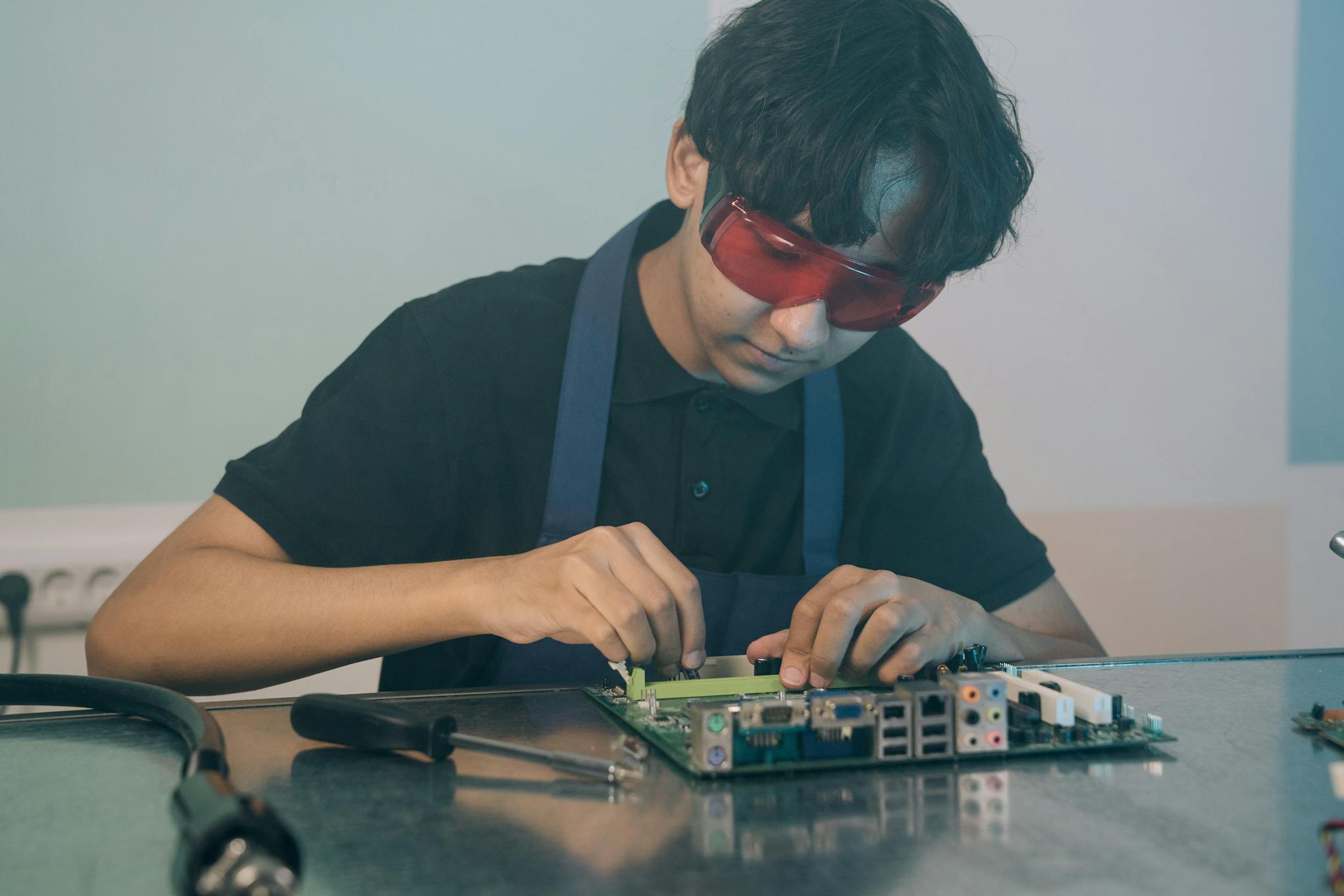 Young technician working with precision on a circuit board, demonstrating focused attention and technical skill indoors.